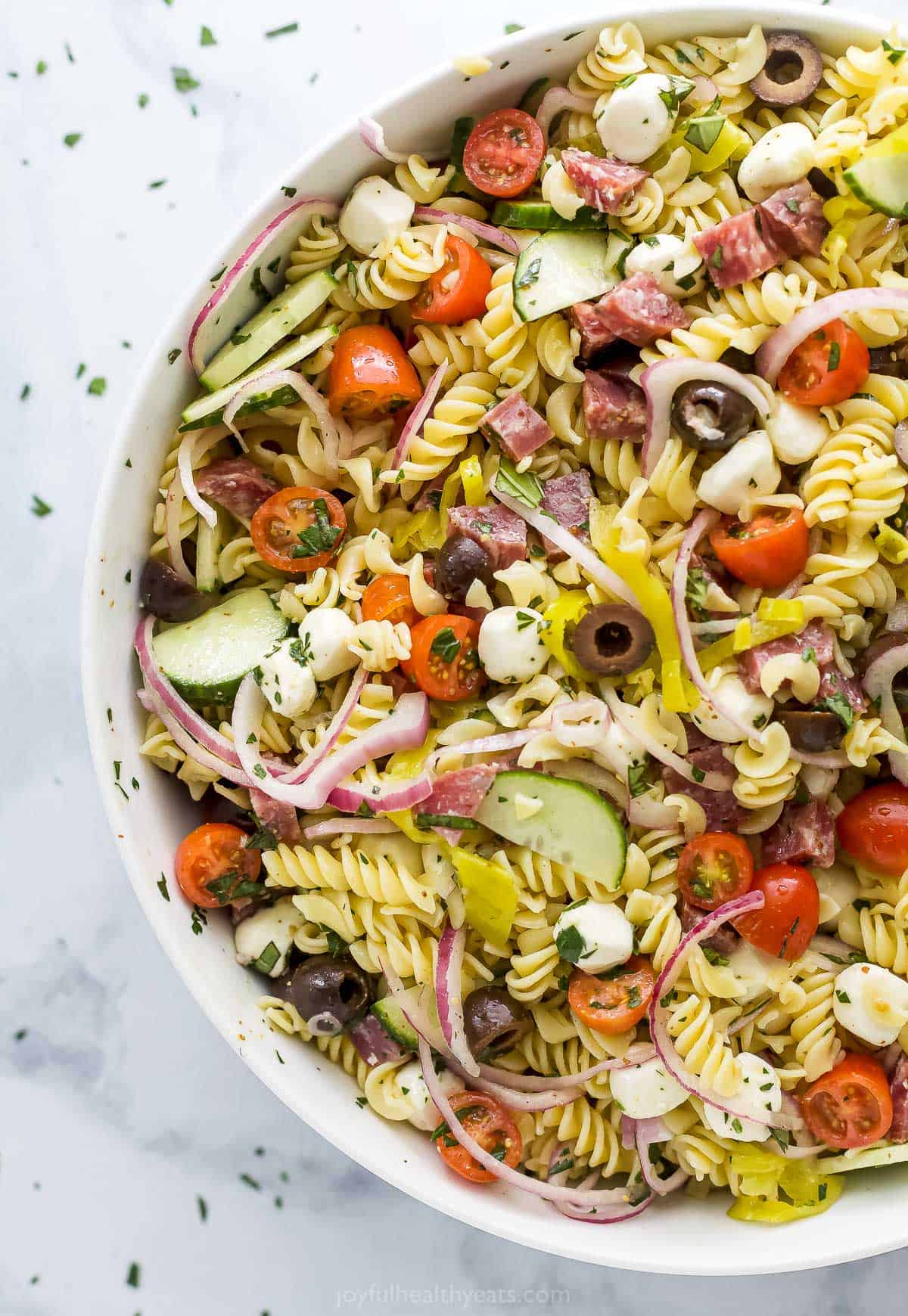 A large bowl of pasta salad on a marble kitchen countertop
