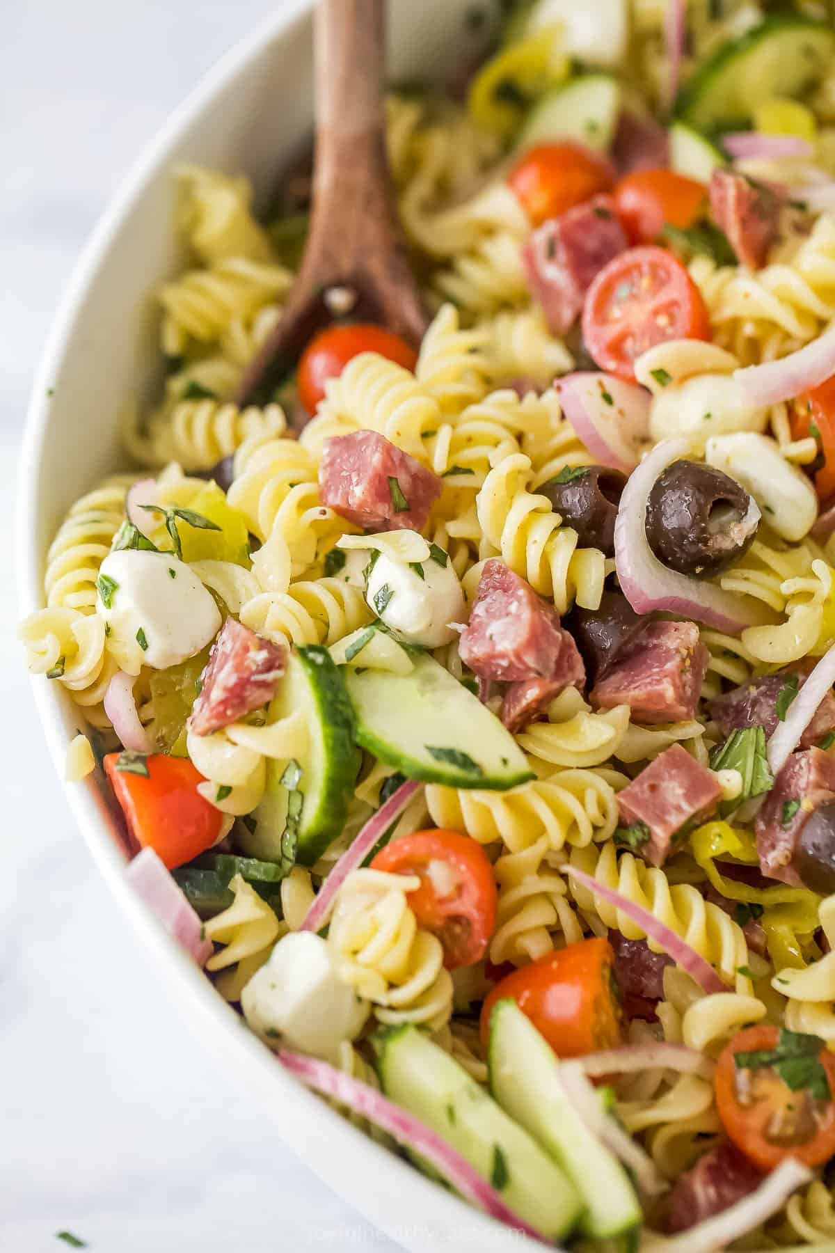 Homemade pasta salad being mixed by a wooden spoon
