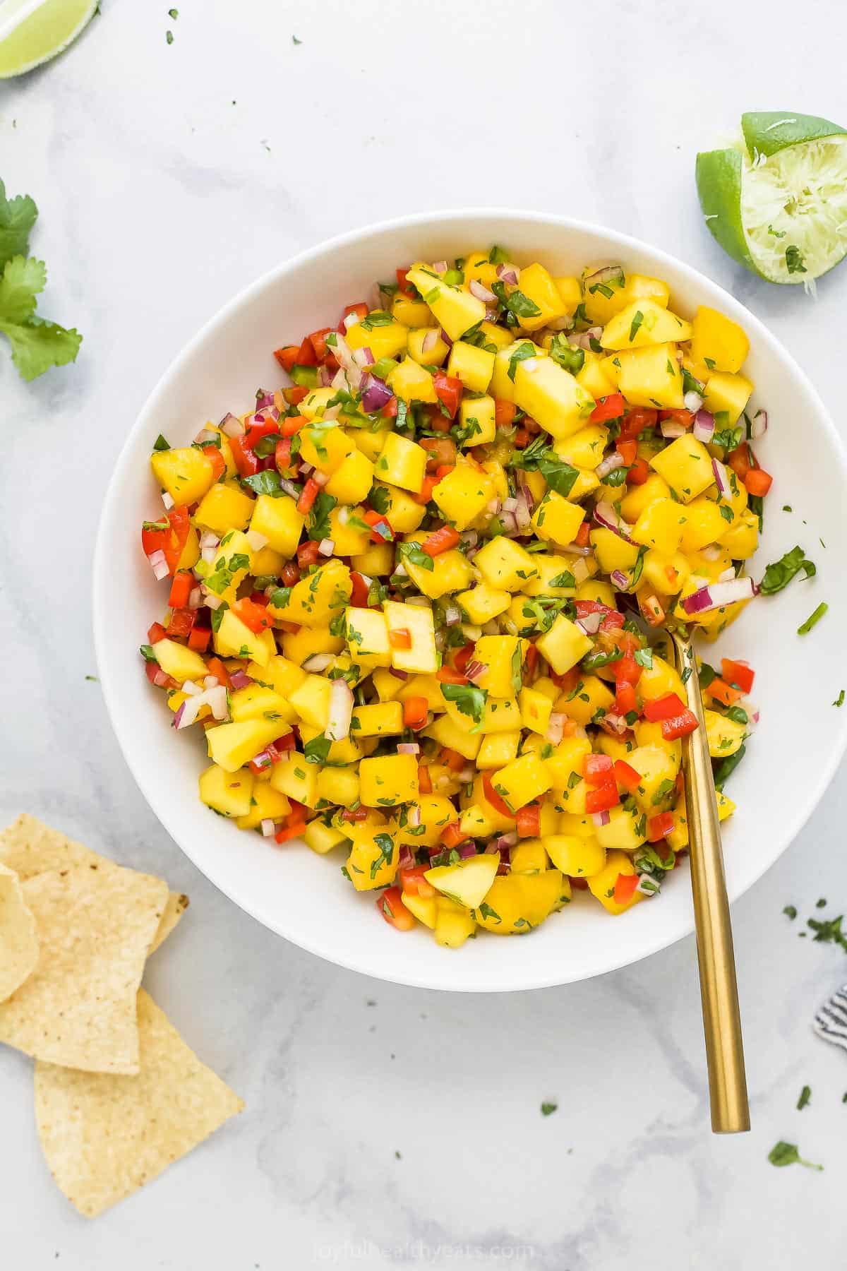 Homemade mango salsa in a bowl with a golden spoon stirring it gently