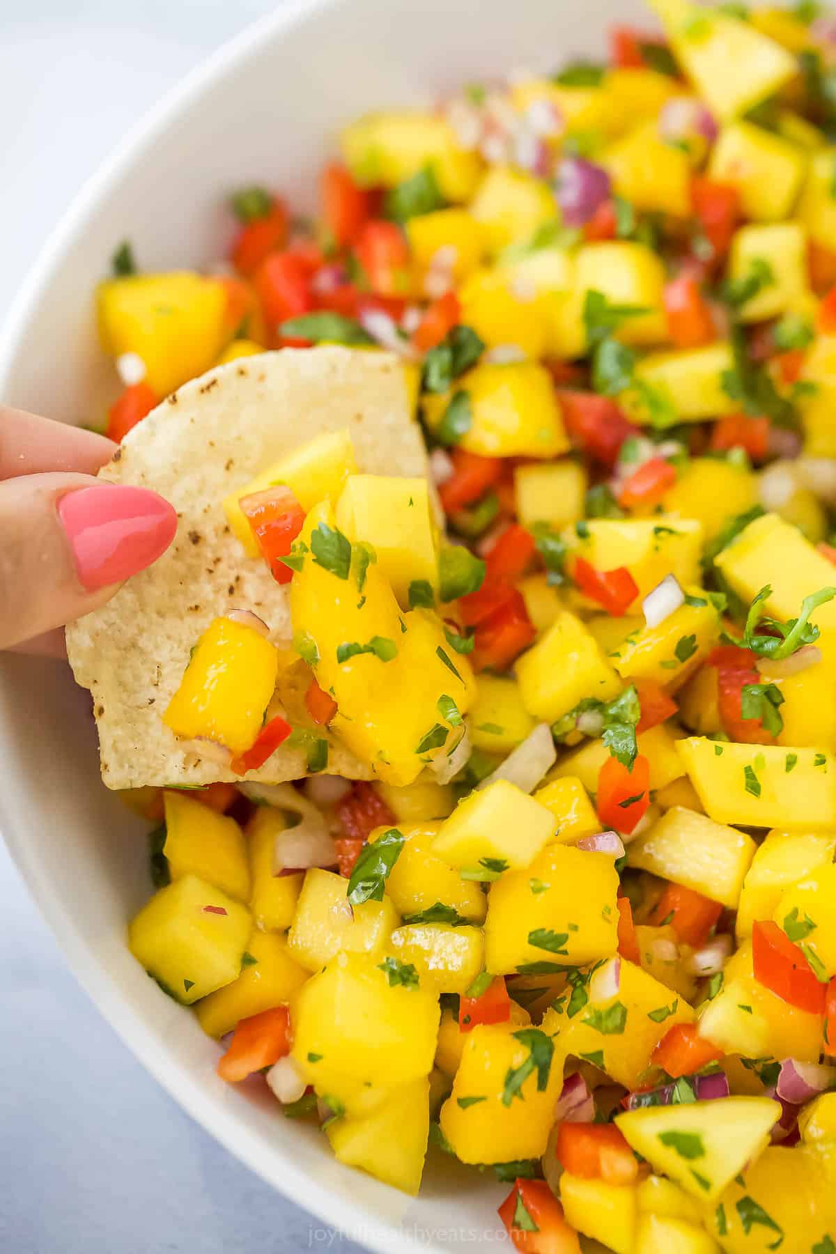 A close-up shot of a tortilla chip being dunked into a bowl of mango salsa