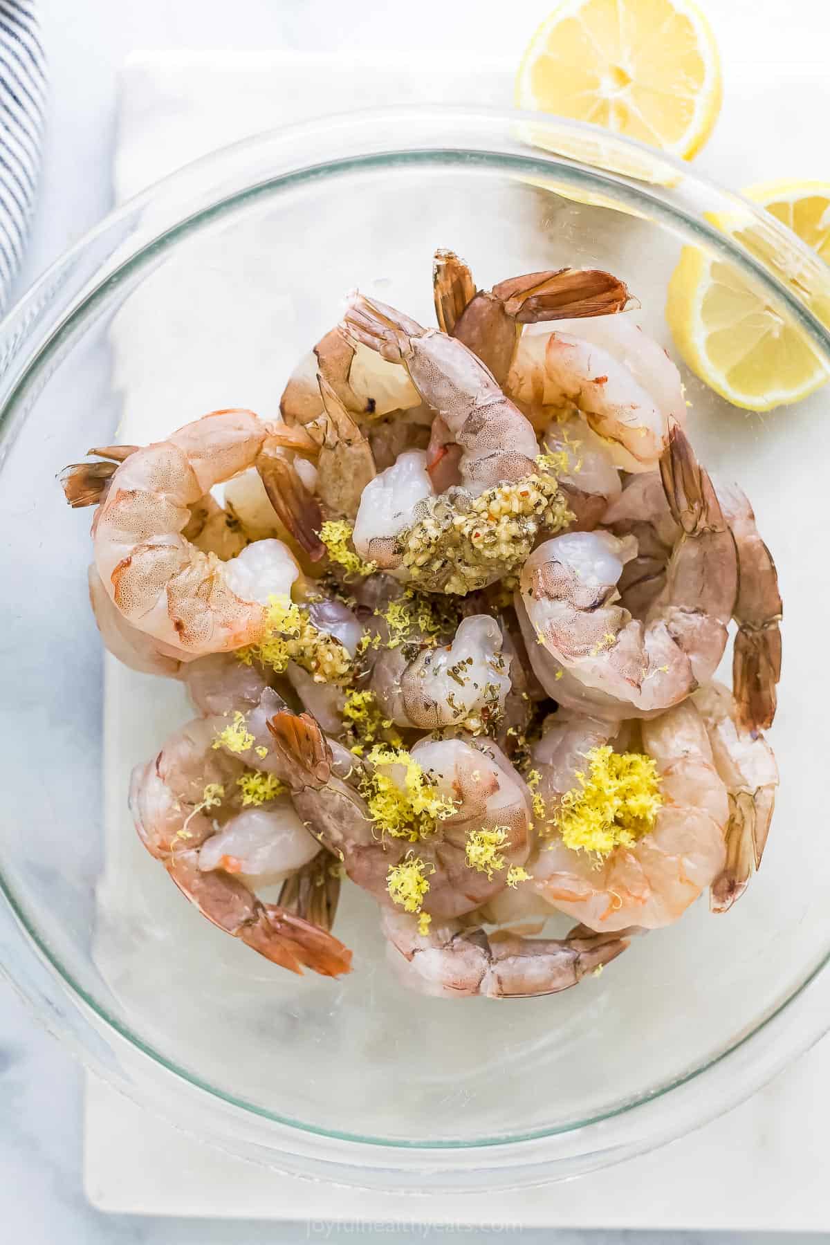 A bowl full of raw shrimp and all of the garlic lemon seasonings