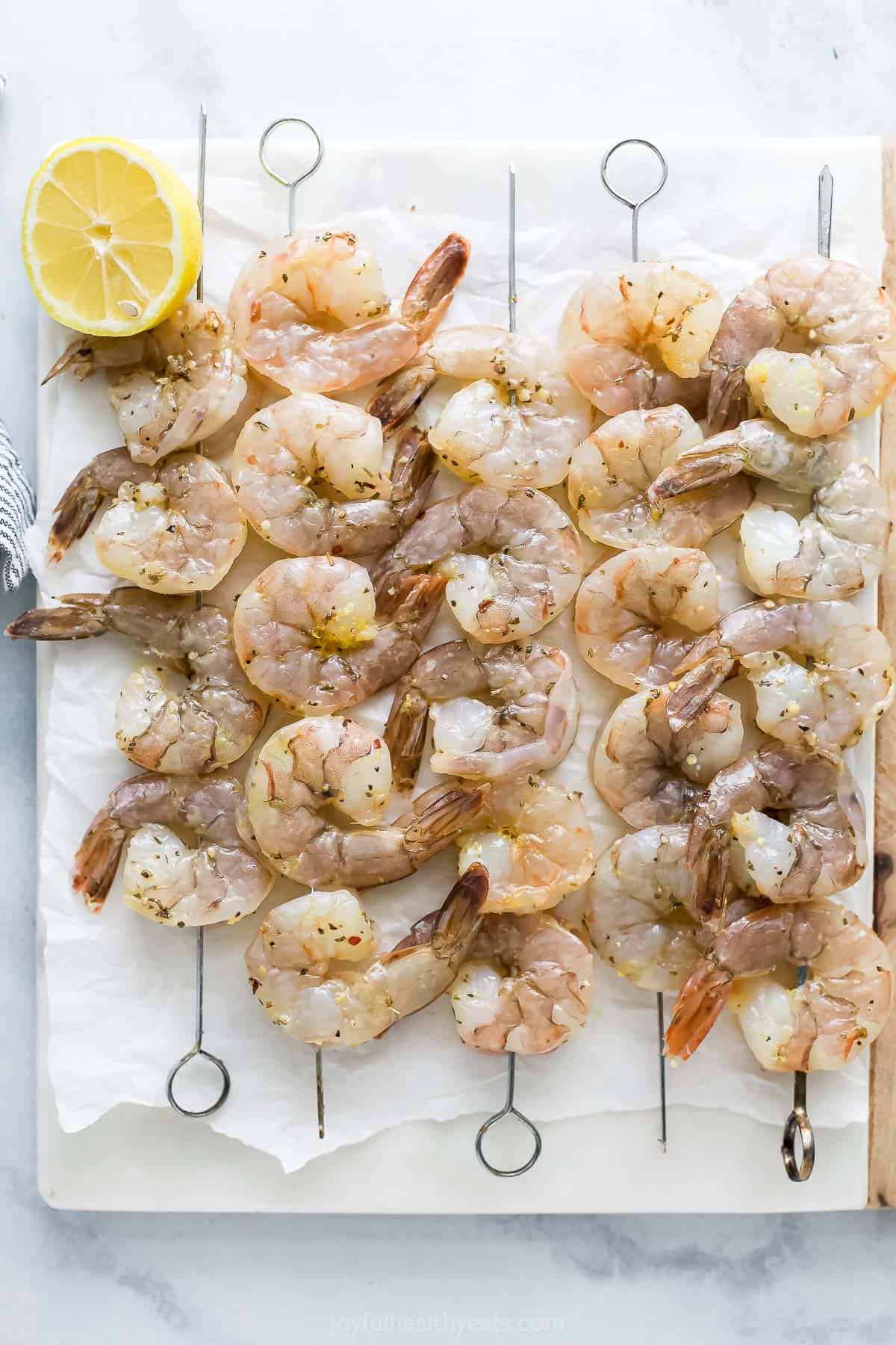 Seasoned raw shrimp threaded onto skewers and resting on top of a parchment-lined cutting board