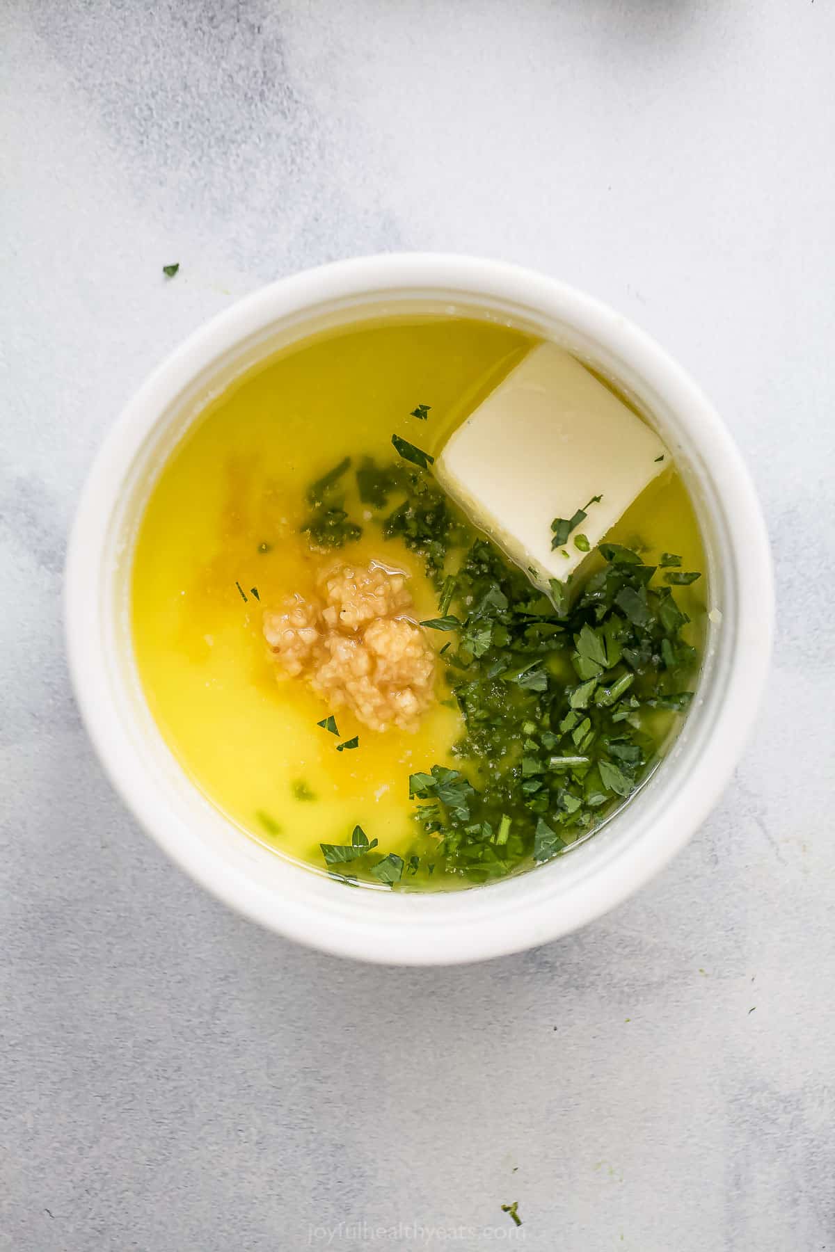 Parsley, butter, salt and garlic inside of a small bowl on a kitchen countertop