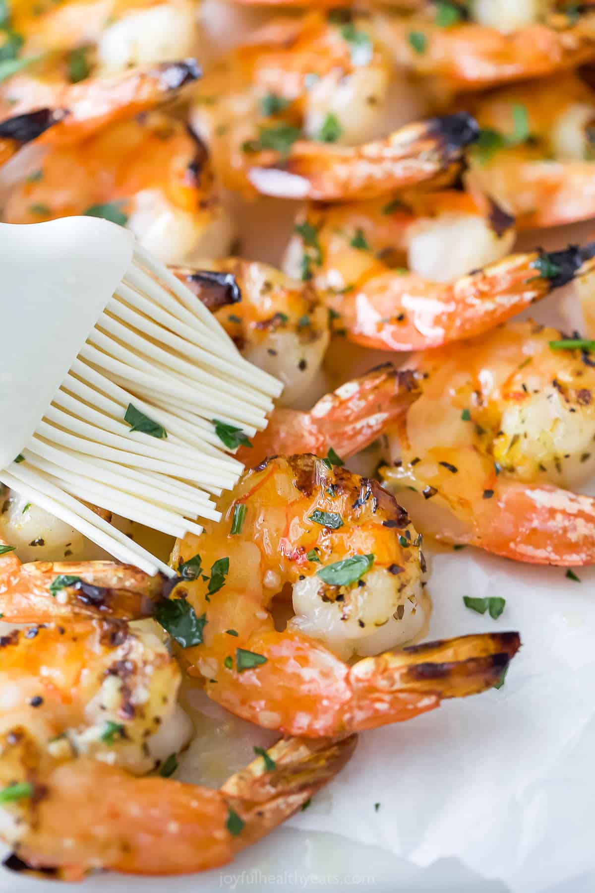 A close-up shot of garlic butter being brushed onto grilled shrimp