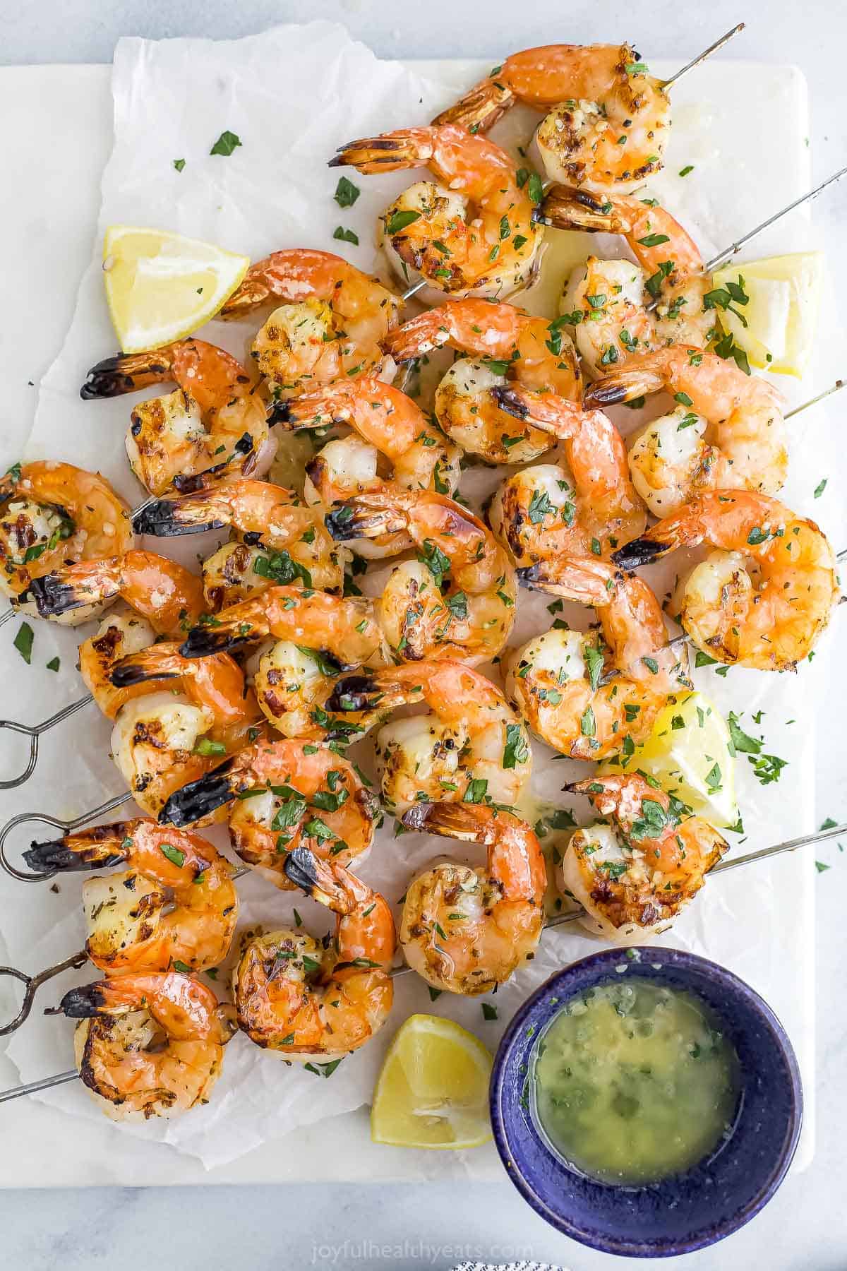 A bunch of skewers of grilled shrimp on a sheet of parchment paper placed on a marble countertop