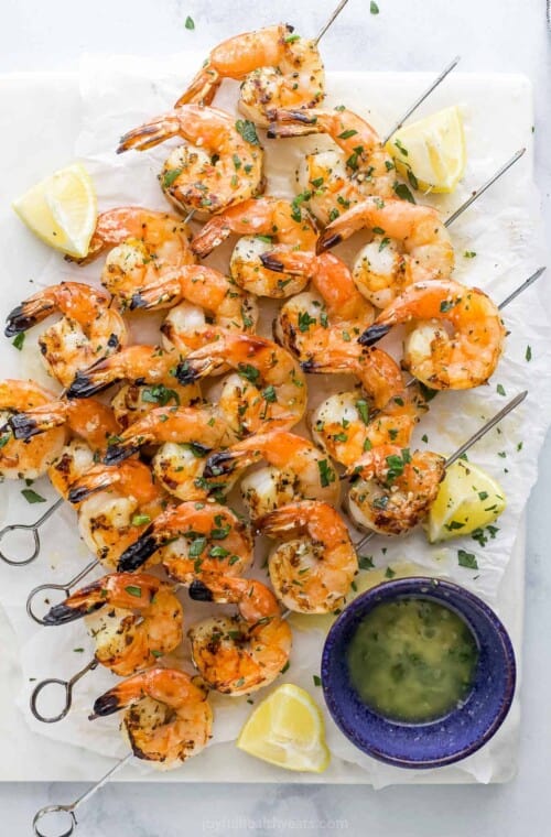 Garlic lemon shrimp on a piece of parchment paper beside a small bowl full of homemade garlic butter