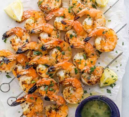 Garlic lemon shrimp on a piece of parchment paper beside a small bowl full of homemade garlic butter