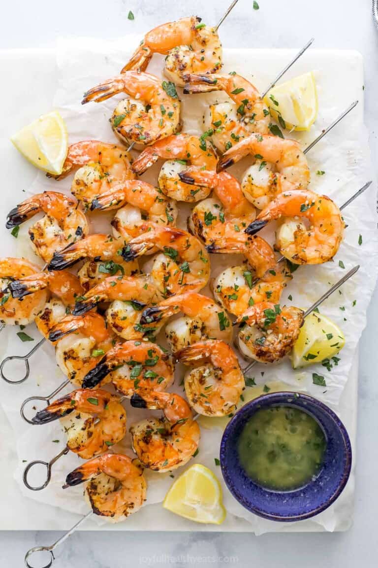 Garlic lemon shrimp on a piece of parchment paper beside a small bowl full of homemade garlic butter