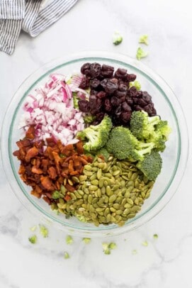 Pepitas, dried cranberries, diced onions and the rest of the salad ingredients inside of a glass bowl