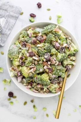 An overhead shot of a bowl of broccoli salad beside a striped dishtowel