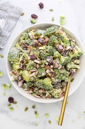 An overhead shot of a bowl of broccoli salad beside a striped dishtowel