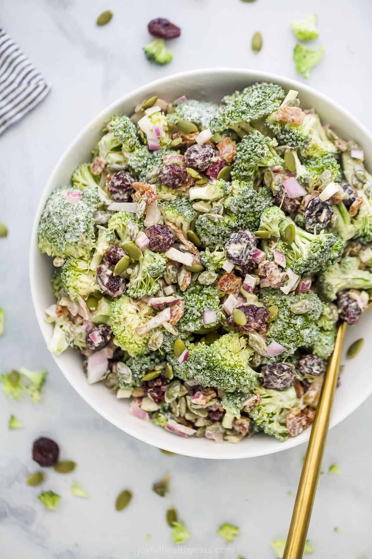 A big bowl of broccoli salad sitting on a marble kitchen countertop