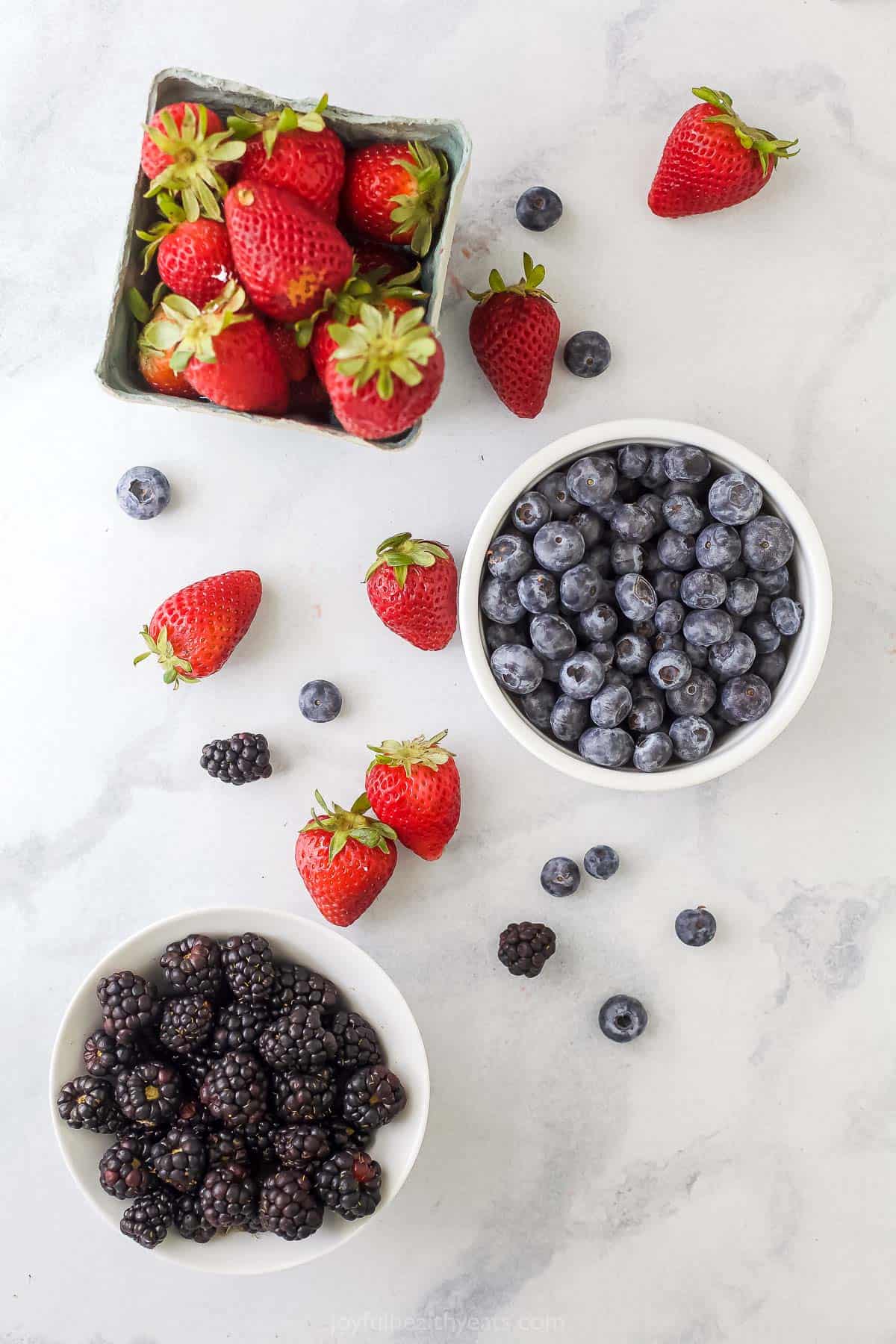 Fresh strawberries, blueberries and blackberries in separate containers on a kitchen countertop