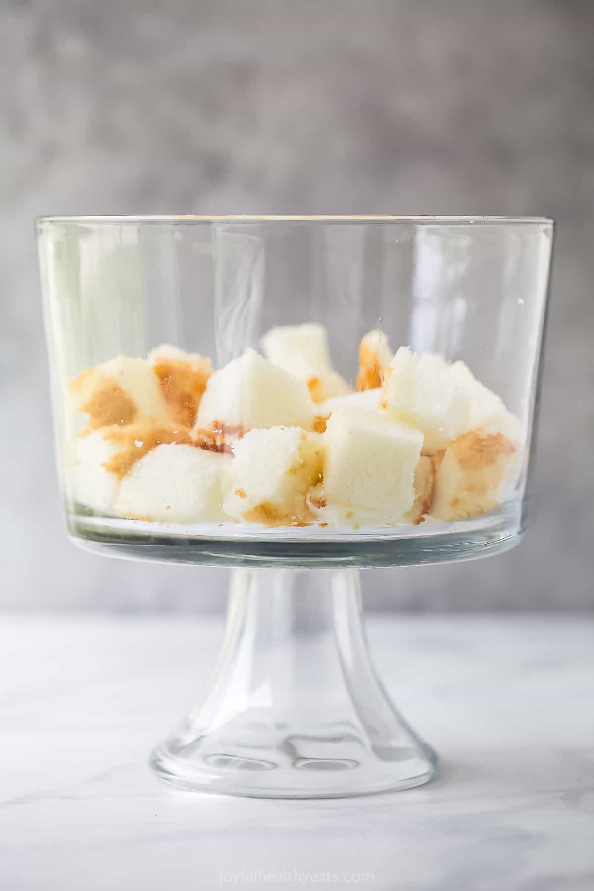 A base layer of angel food cake cubes inside of a clear trifle dish