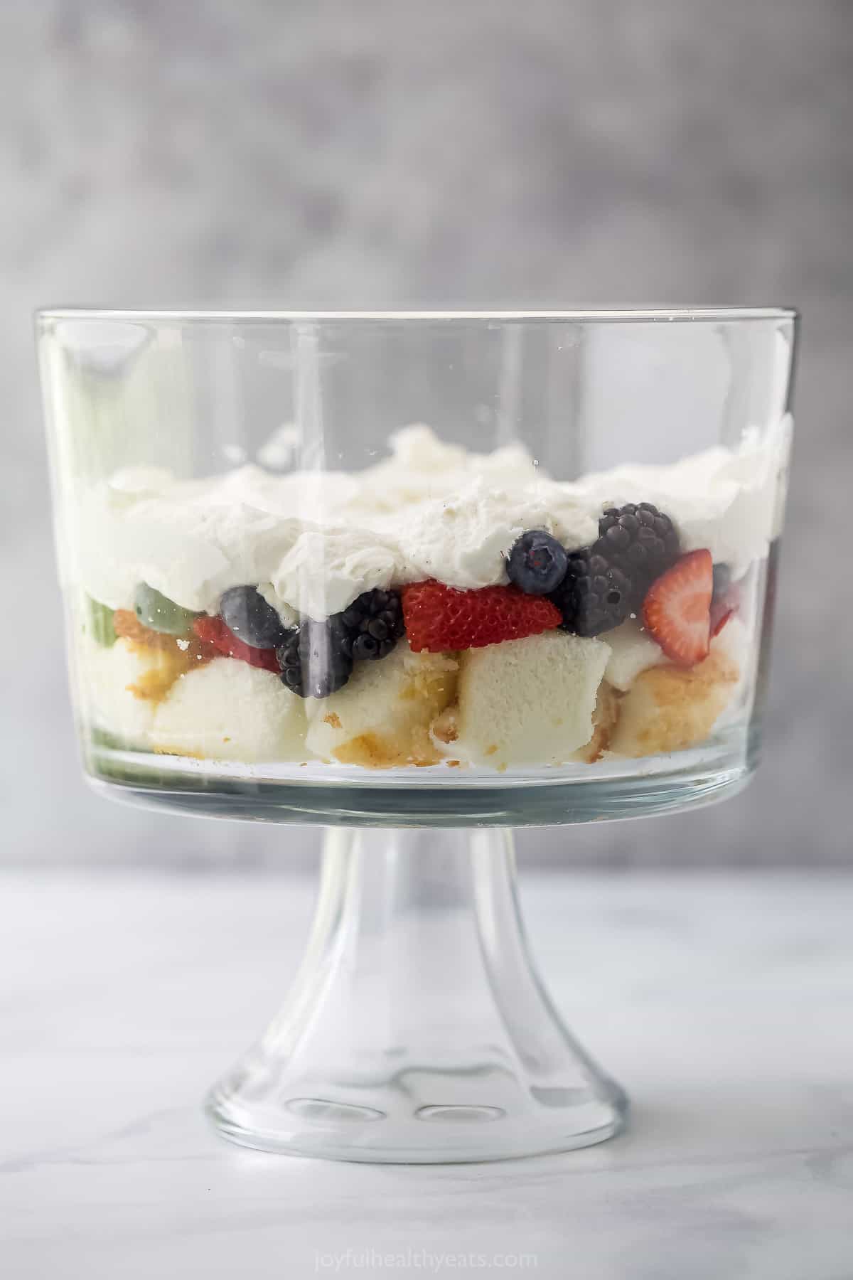 Half of a strawberry shortcake trifle layered into a big glass trifle dish