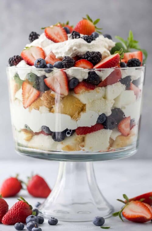 A large trifle dish with layers of angel food cake, fresh berries and homemade whipped cream inside