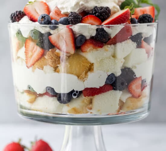 A large trifle dish with layers of angel food cake, fresh berries and homemade whipped cream inside