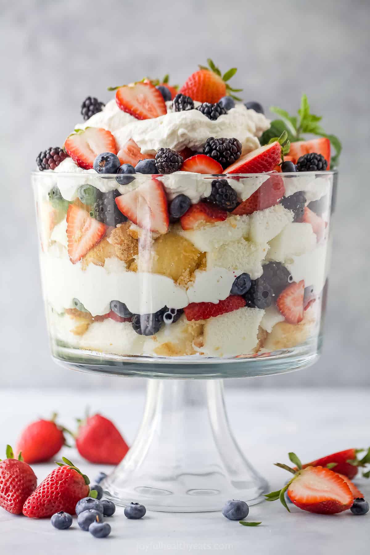 A layered dessert with fresh berries, angel food cake and whipped cream in a large glass container