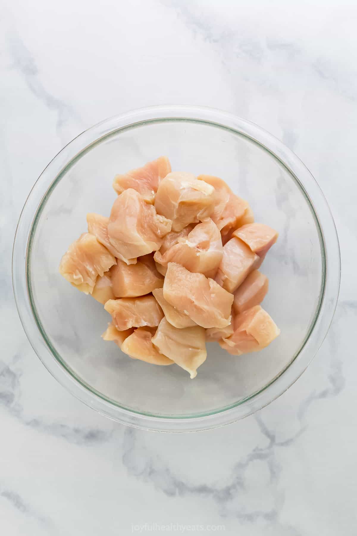 Raw cubes of boneless, skinless chicken in a glass bowl on a kitchen countertop
