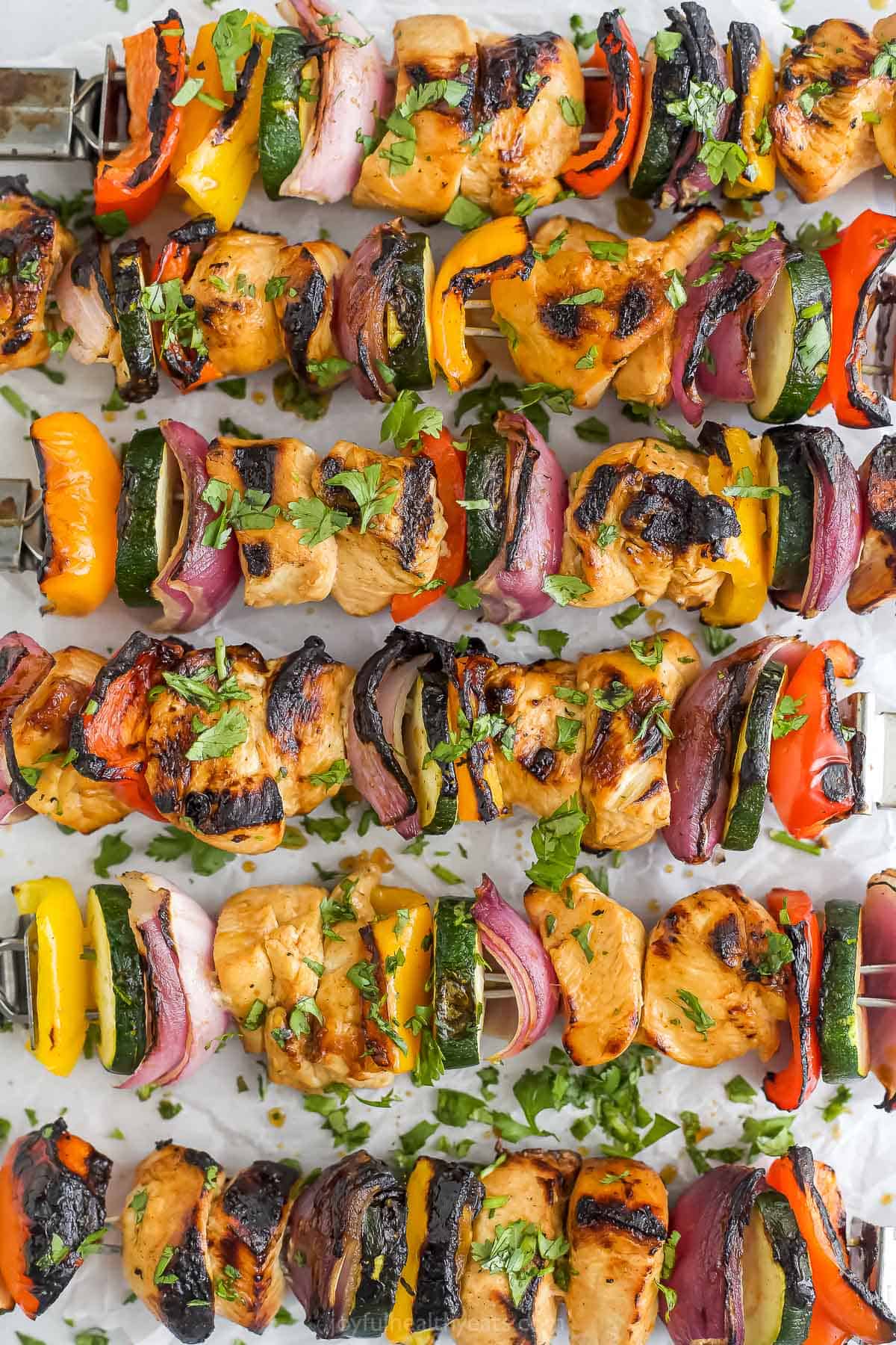 Six pineapple marinated chicken kabobs lined up on a sheet of parchment paper
