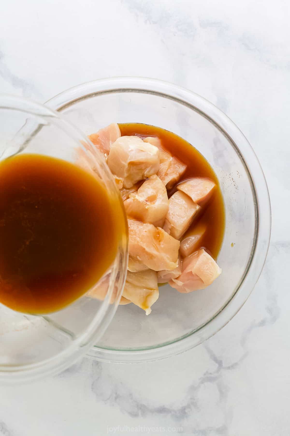 Marinade being poured over cubed chicken in a bowl