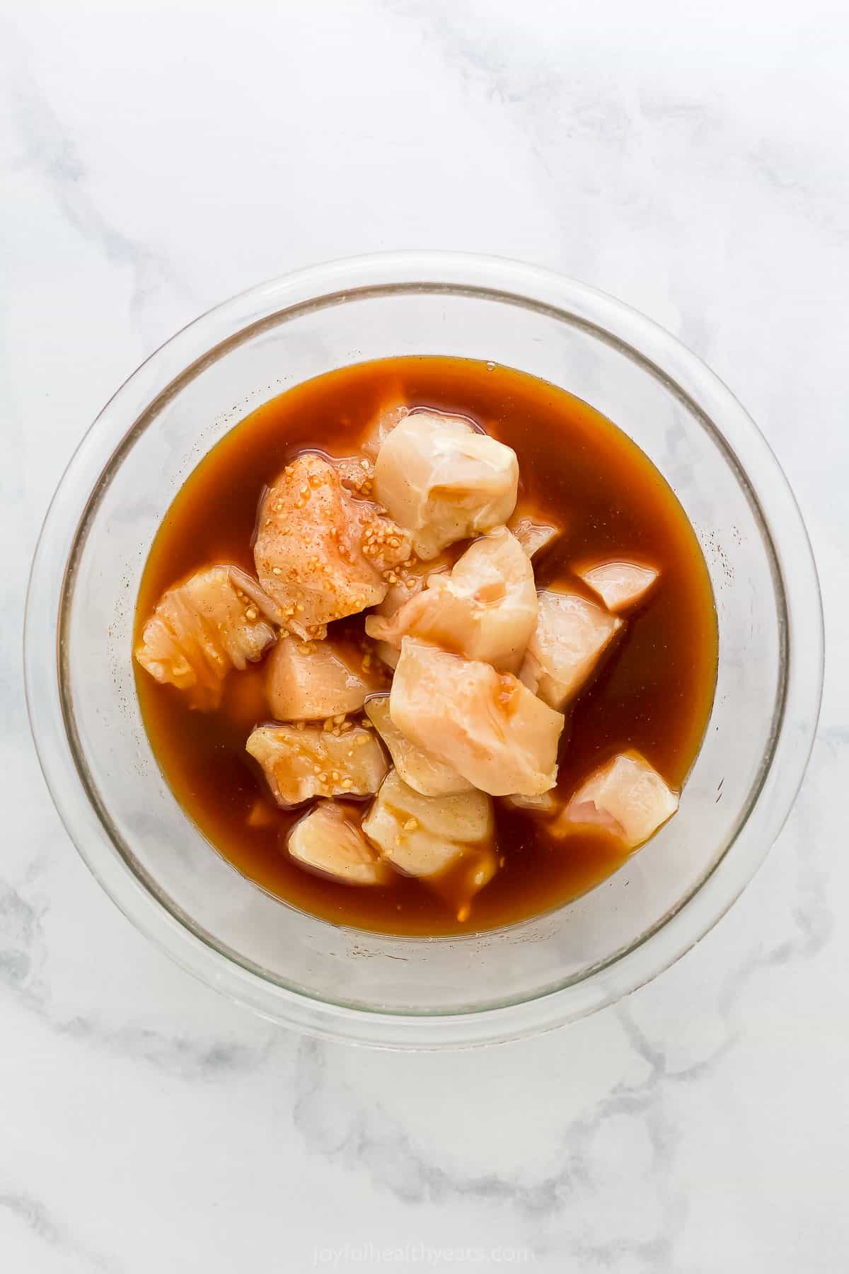 Cubes of boneless, skinless chicken in a glass bowl with homemade pineapple marinade