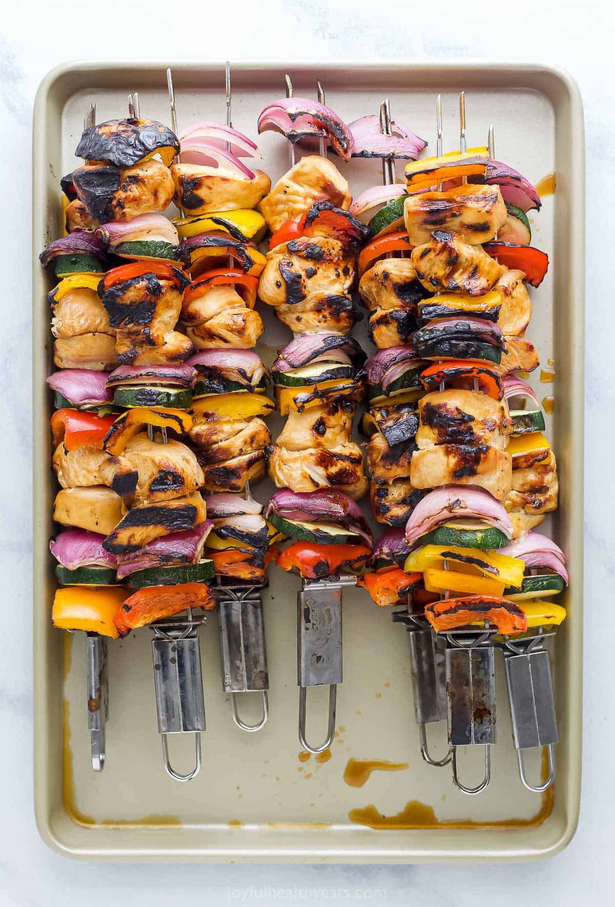 A metal baking sheet with grilled chicken kabobs piled onto it