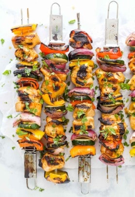 Four grilled chicken kabobs lined up on a countertop with a fifth one partially in frame