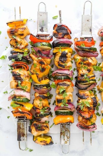 Four grilled chicken kabobs lined up on a countertop with a fifth one partially in frame
