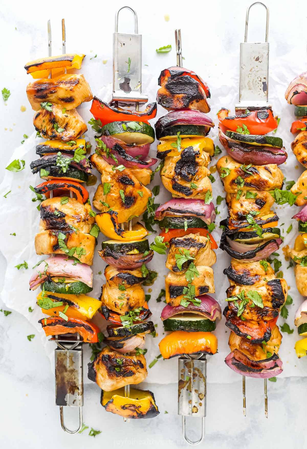 Four grilled chicken kabobs lined up on a countertop with a fifth one partially in frame