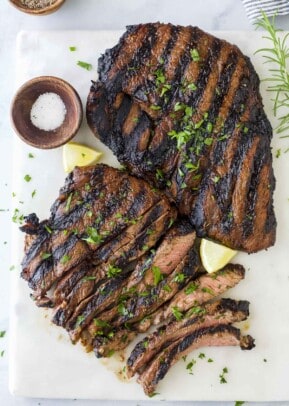 Two sirloin steaks on a cutting board with fresh herbs and a small dish of salt