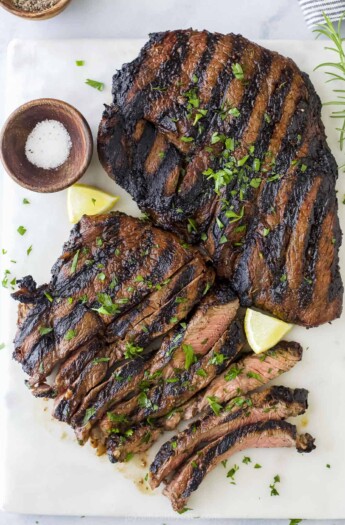 Two sirloin steaks on a cutting board with fresh herbs and a small dish of salt