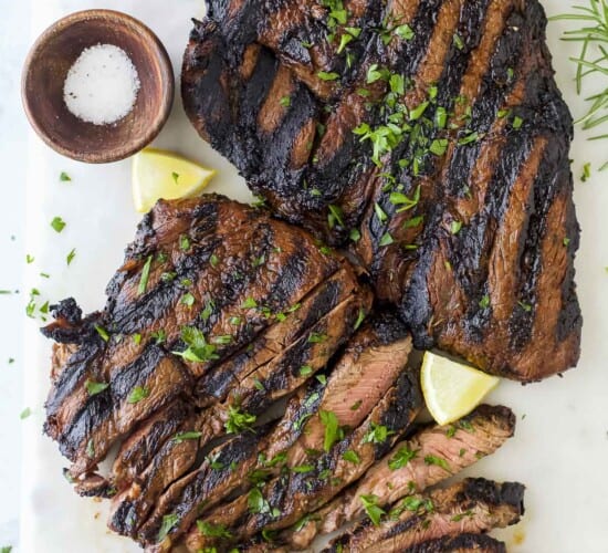 Two sirloin steaks on a cutting board with fresh herbs and a small dish of salt