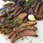 Slices of grilled beef on a plastic cutting board with fresh lemon wedges