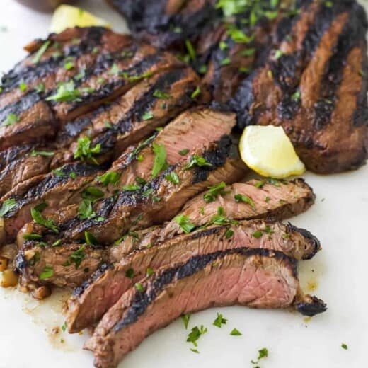 Slices of grilled beef on a plastic cutting board with fresh lemon wedges
