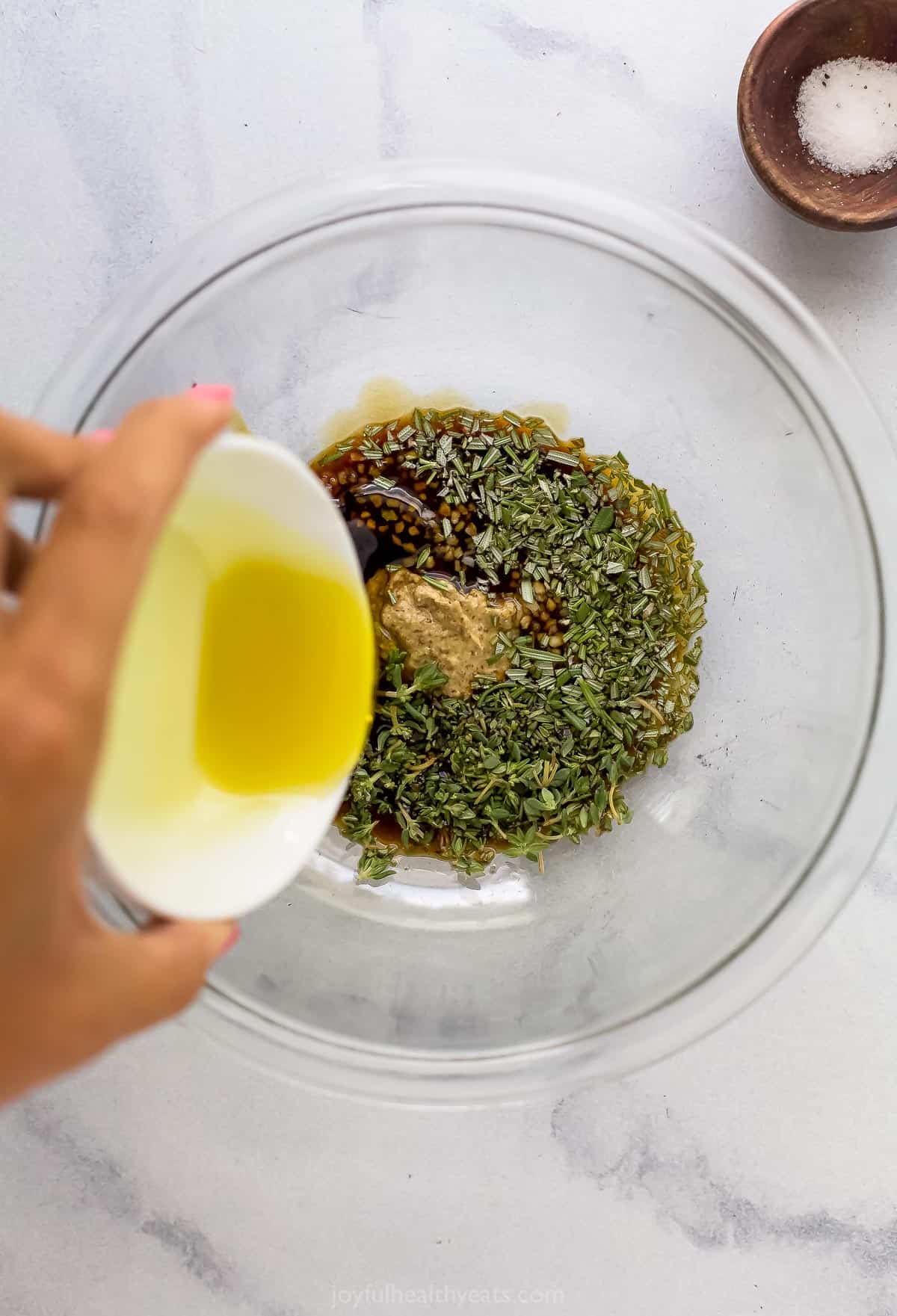 Olive oil being poured into a mixing bowl full of dijon mustard, tamari sauce, fresh rosemary and the rest of the steak marinade ingredients