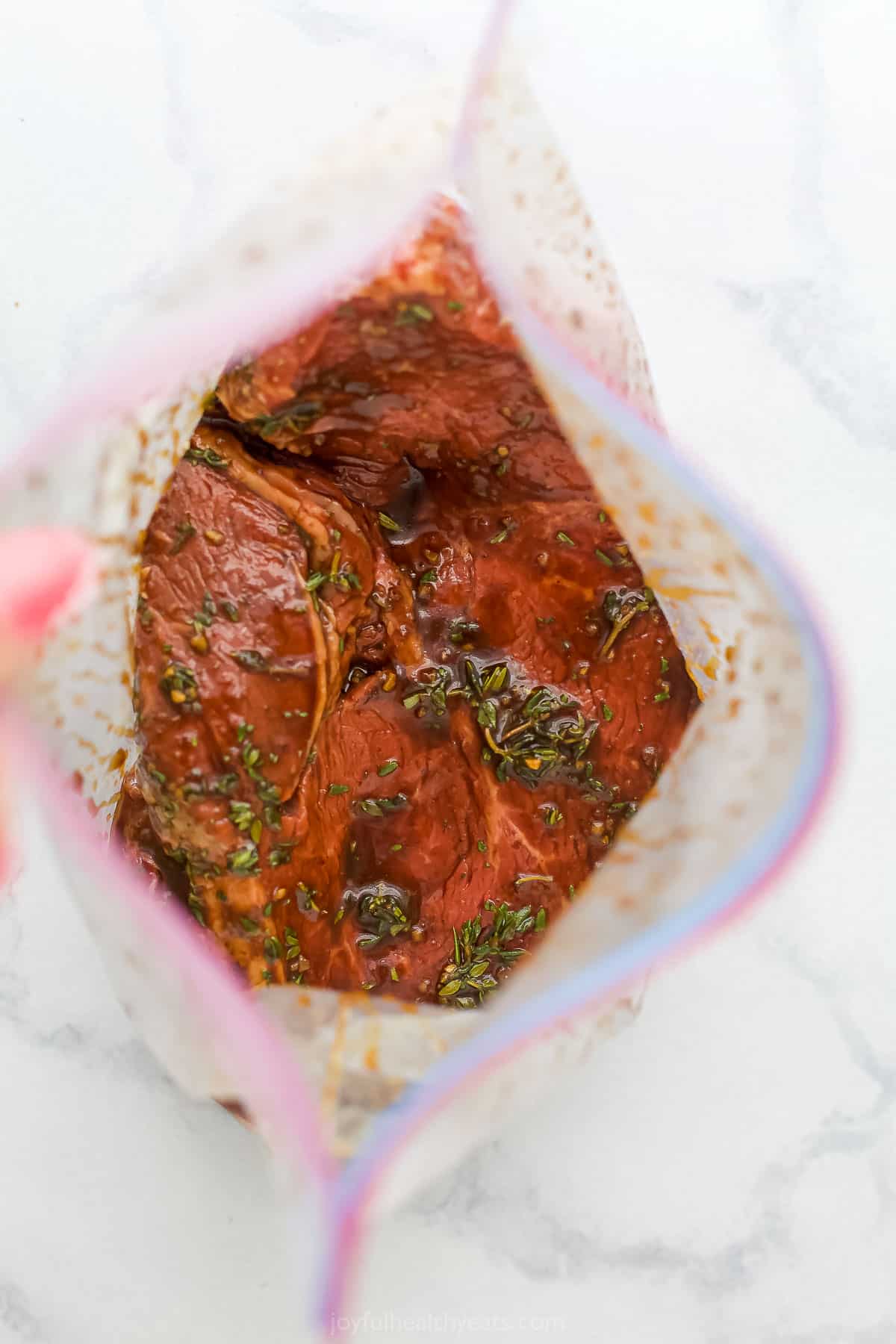 Steak marinating inside of a plastic storage bag on a marble countertop