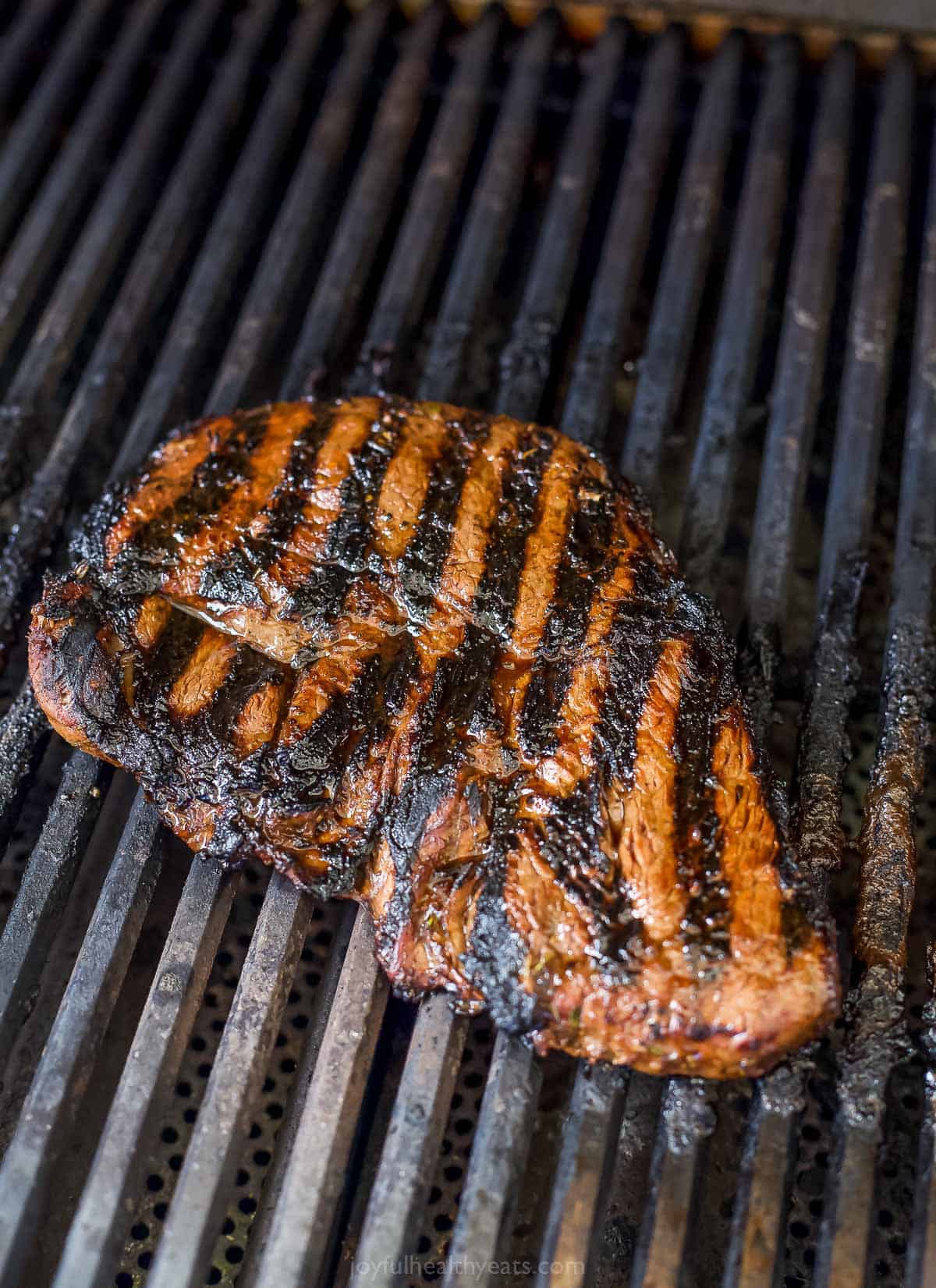 A sirloin steak sitting on a grill with the top side lined with char marks
