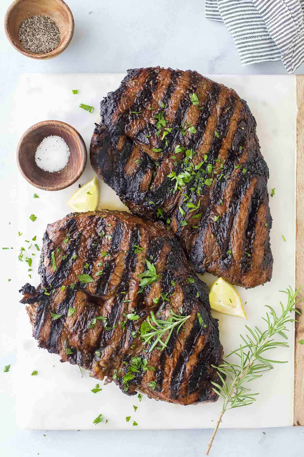 A plastic cutting board holding two freshly grilled steaks before they've been sliced