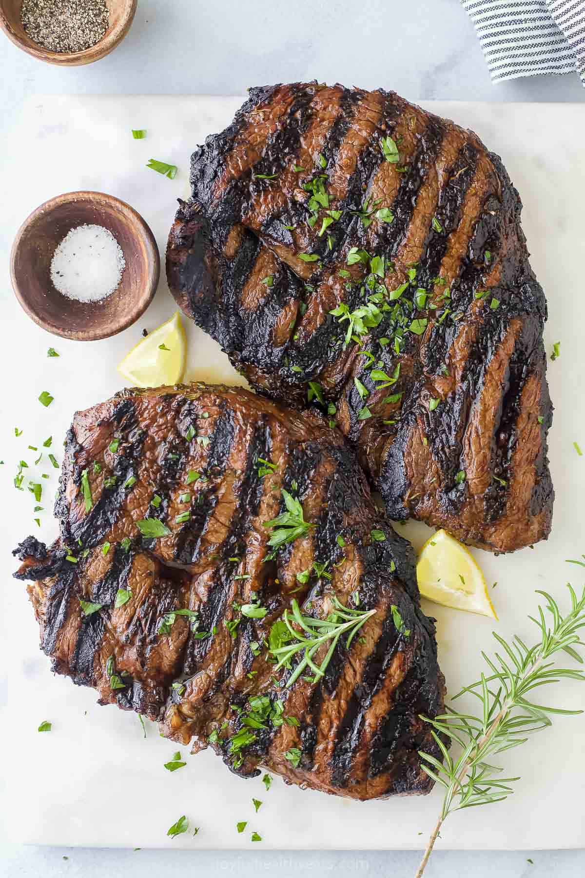 Two top sirloin steaks with char marks on the outsides and chopped herbs on top