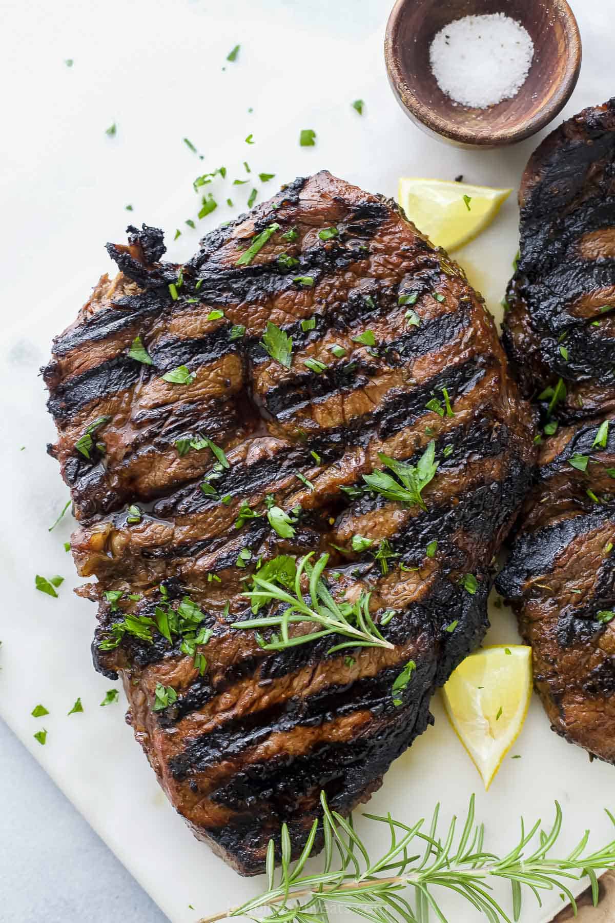 Grilled steak on a cutting board on top of a marble kitchen countertop