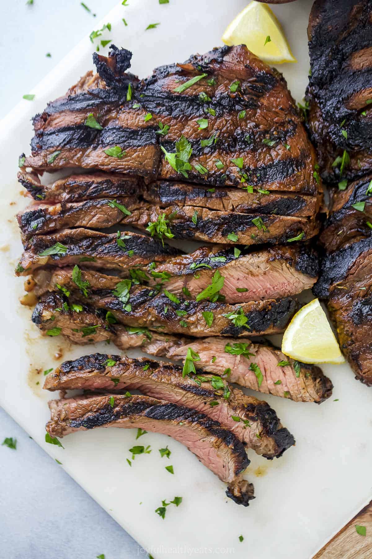 Sliced beef on a white cutting board with chopped parsley sprinkled on top