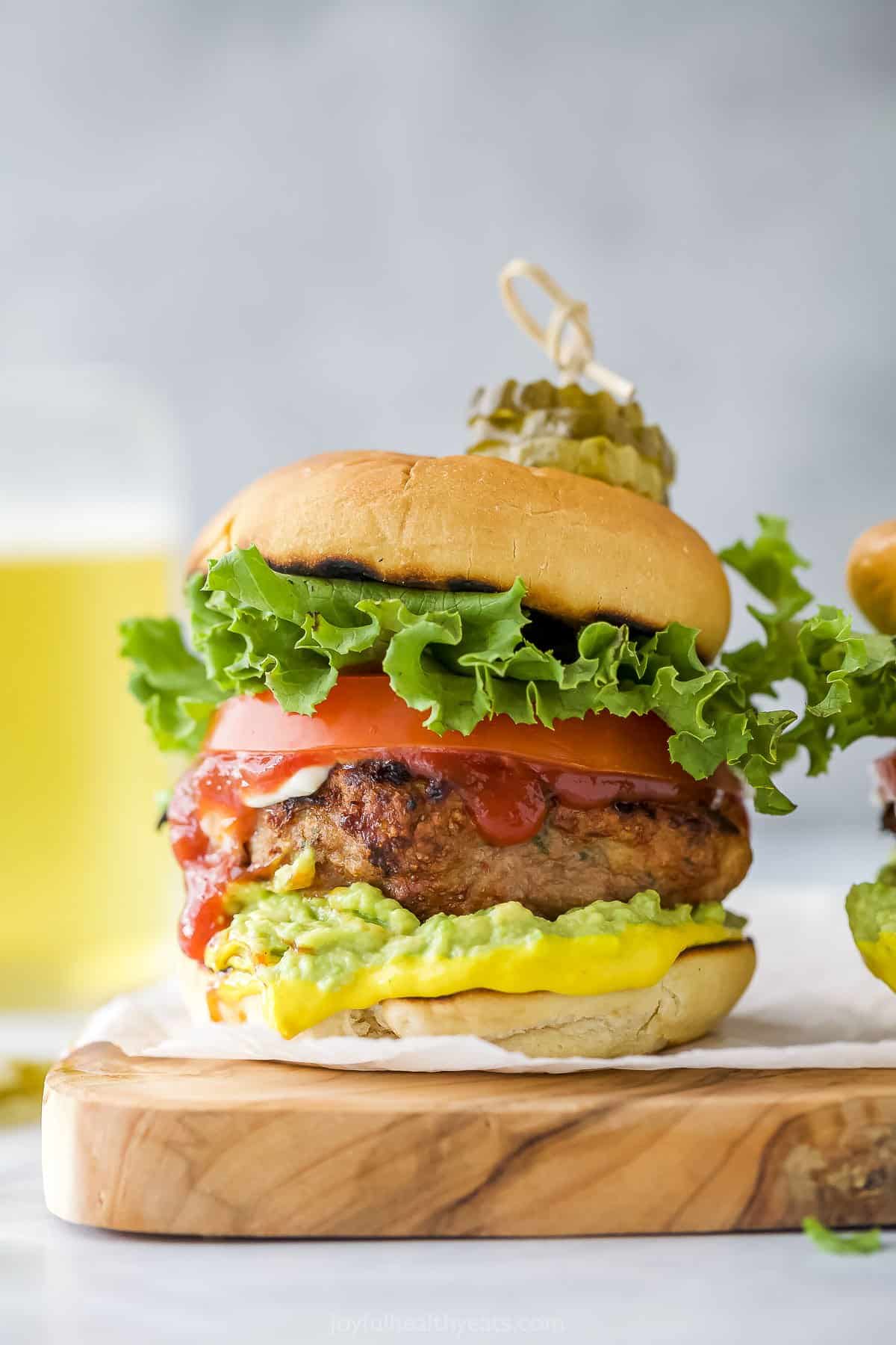 A homemade burger on a wooden cutting board with a glass of beer behind it