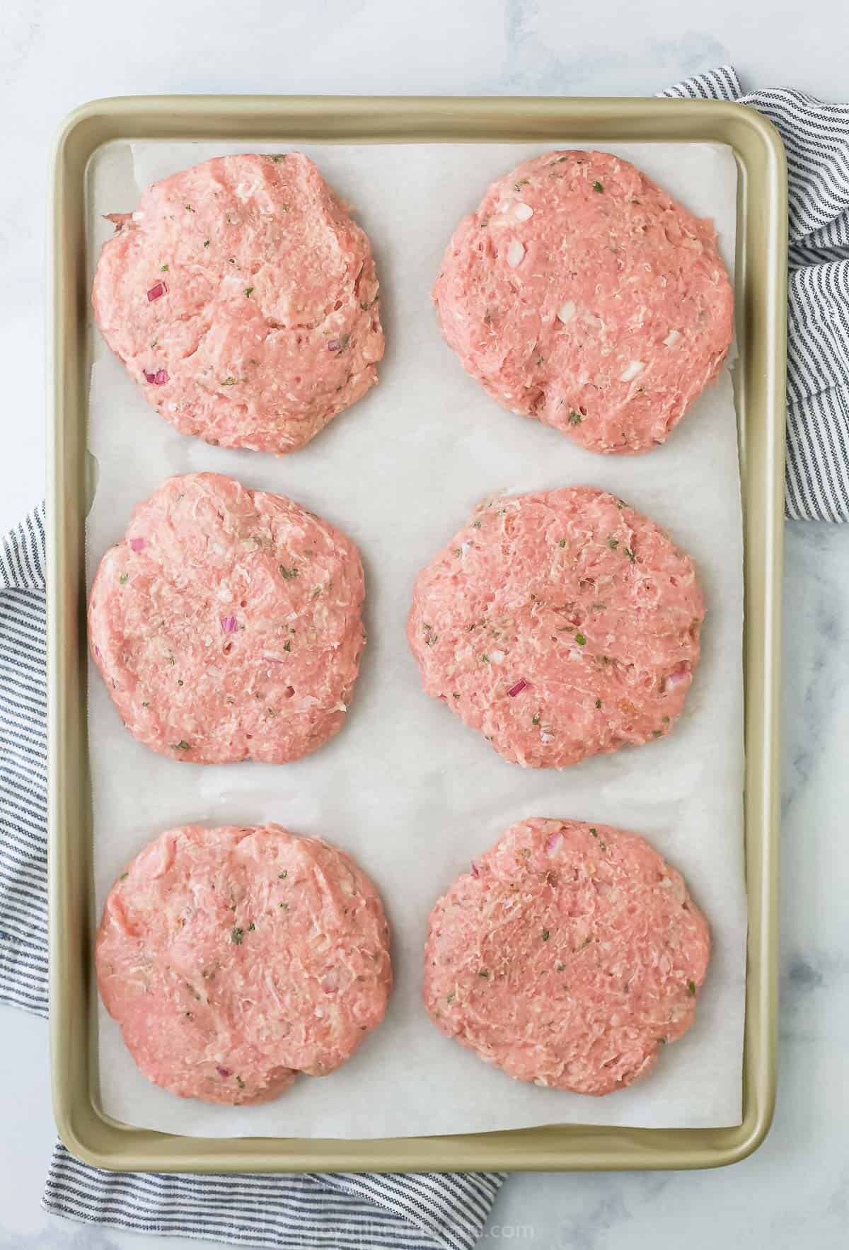 Six raw turkey patties on a cookie sheet lined with parchment paper