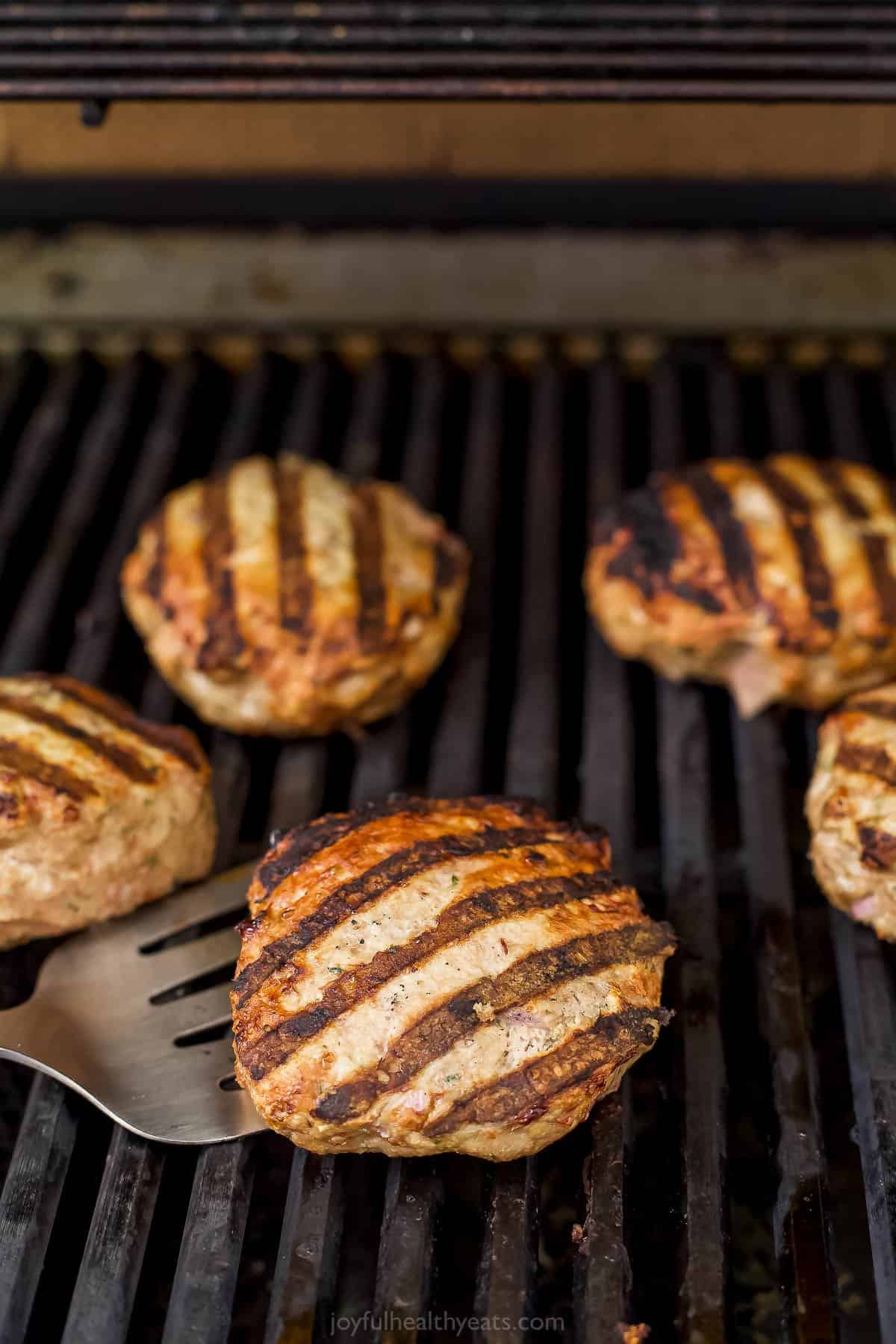 A turkey patty cooking on a grill with a metal spatula slid underneath it to flip it over