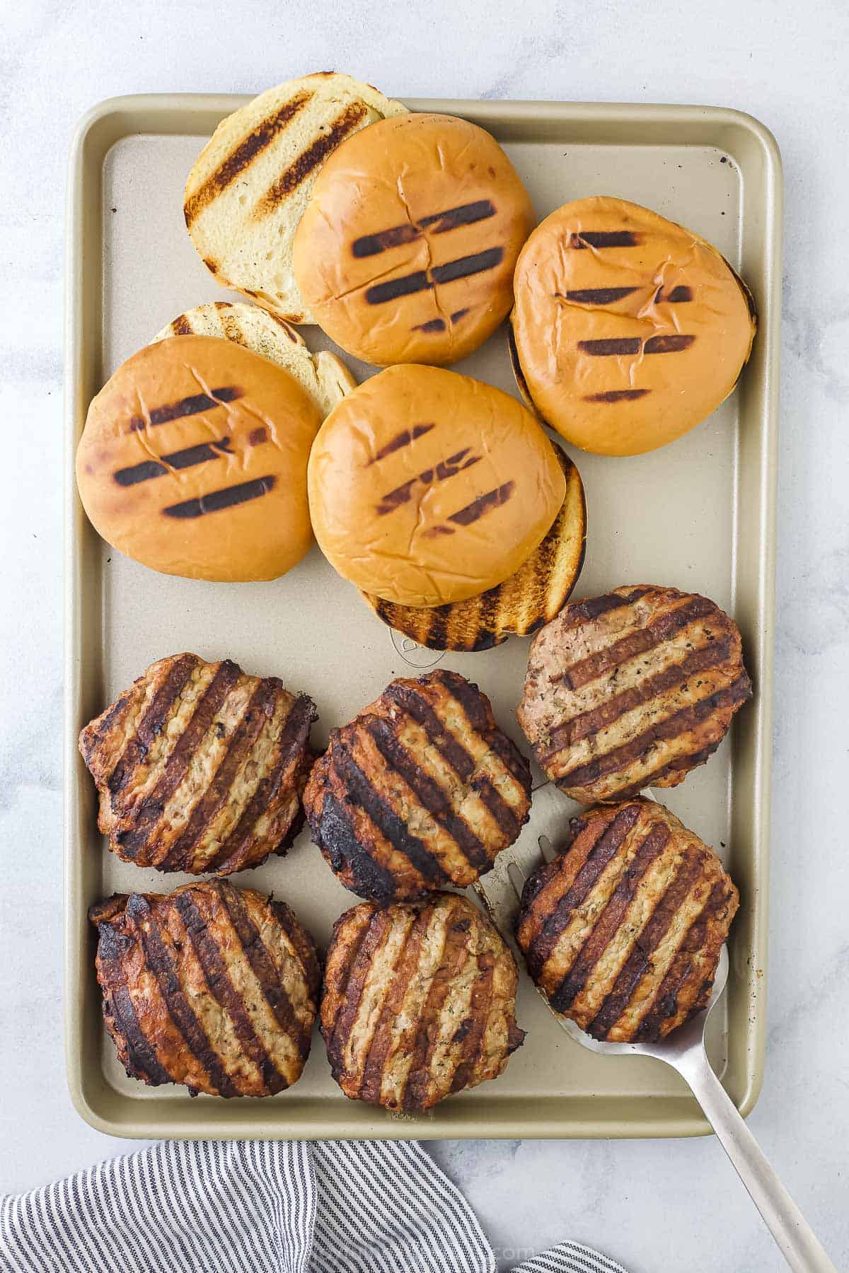 Grilled turkey patties on a baking sheet beside grilled burger buns