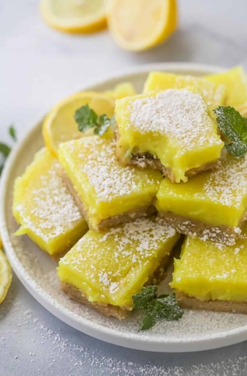 A batch of vegan lemon bars piled onto a plate with a raised rim