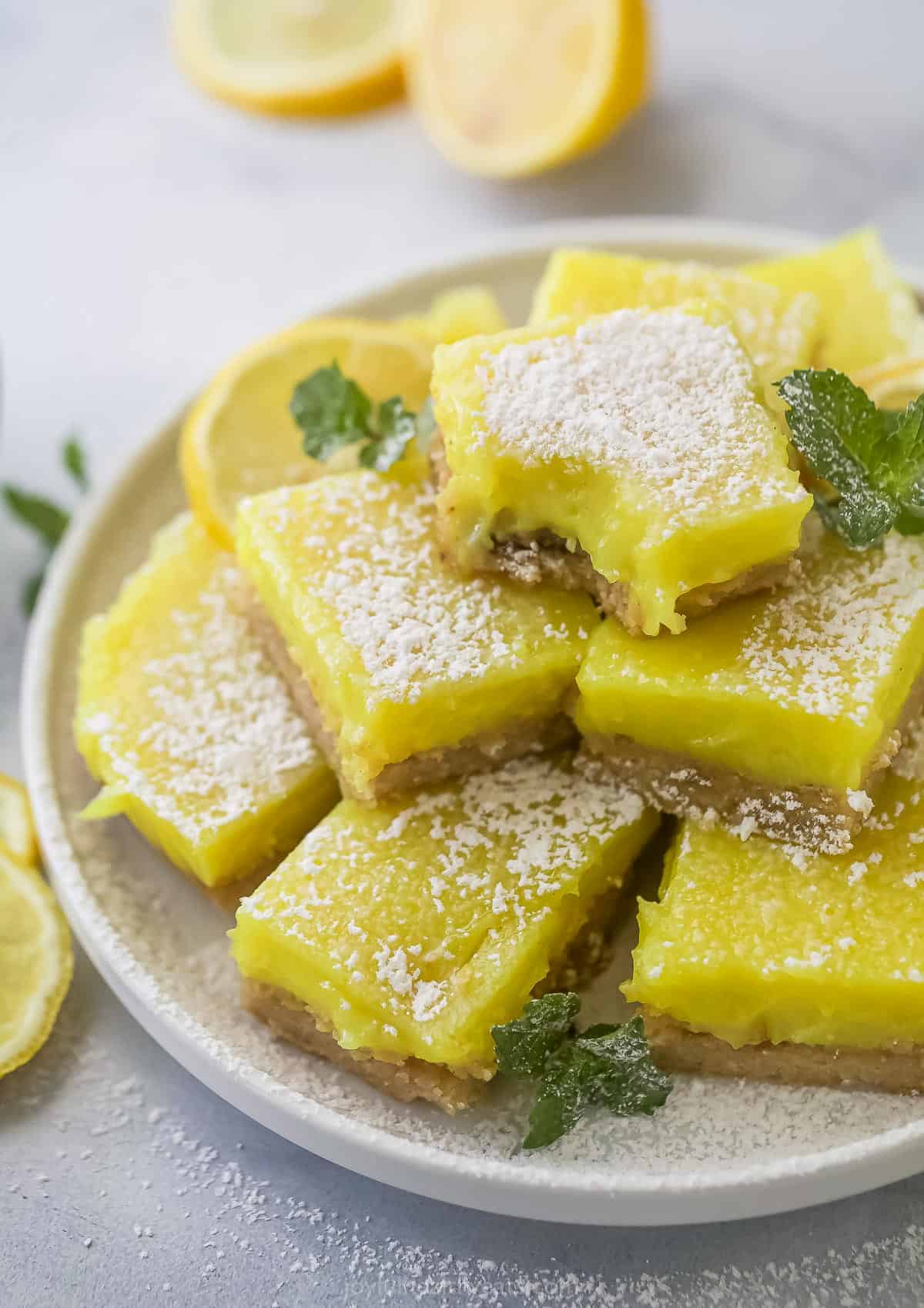 A batch of vegan lemon bars piled onto a plate with a raised rim