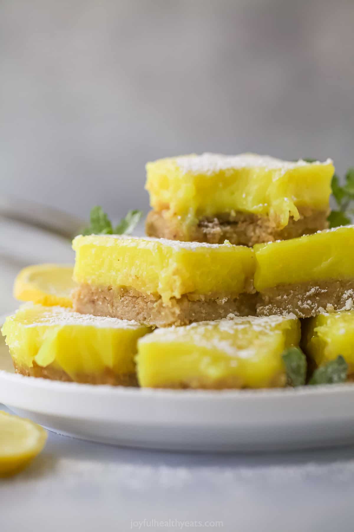 Vegan and gluten-free lemon bars piled onto a plate on top of a kitchen counter