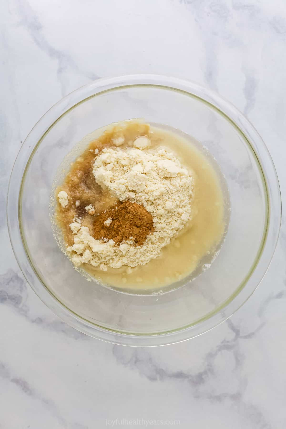 All of the almond crust ingredients inside of a clear mixing bowl on a countertop